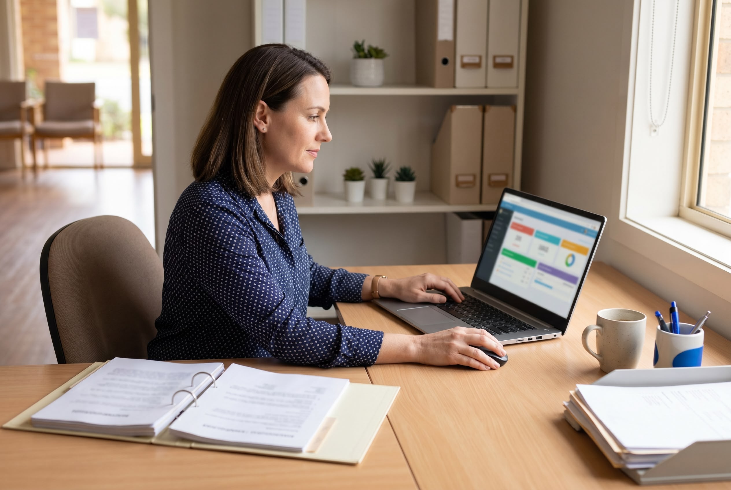 10 skills every Australian practice manager needs in 2026 hero image Australian practice manager working calmly across an open RACGP-style accreditation binder, a clinic dashboard on laptop, and clinic paperwork at a tidy desk