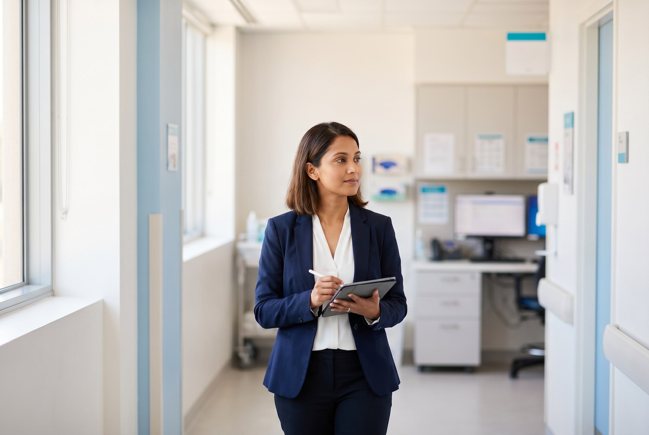 Healthcare quality auditor walking a hospital corridor with a tablet, observing clinical practice as part of a scheduled NSQHS audit