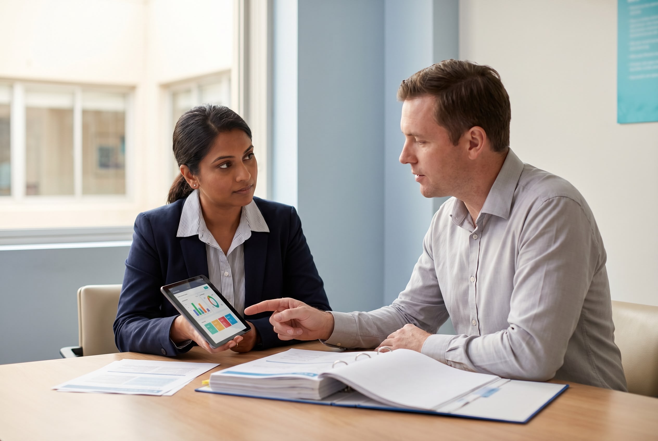Healthcare quality auditor salary in Australia Healthcare quality auditor reviewing audit findings on a tablet with a clinical lead in an Australian hospital meeting room