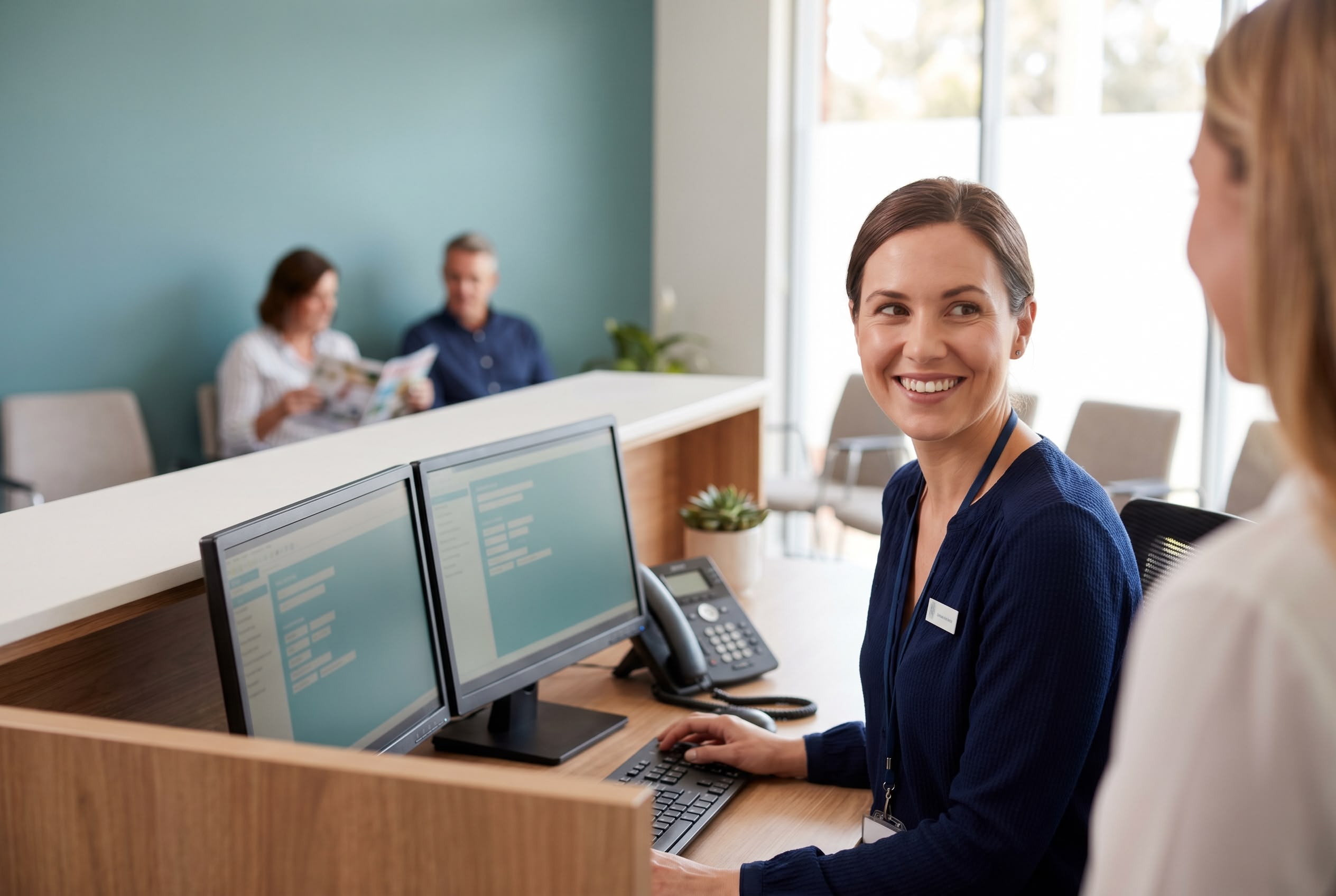 Australian medical receptionist smiling at a patient at a modern general practice front desk